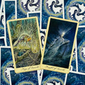 Tarot kortos su auksiniu kraštu, dvi atviros kortos (Page of Swords, Knight of Swords) ant mėlyno nugarėlių fono, arti apžvalgai