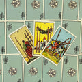 Tarot kortos Rider–Waite stiliaus, trys atverstos kortos (III, IV, V) centre ant žalsvai mėtų nugarėlių