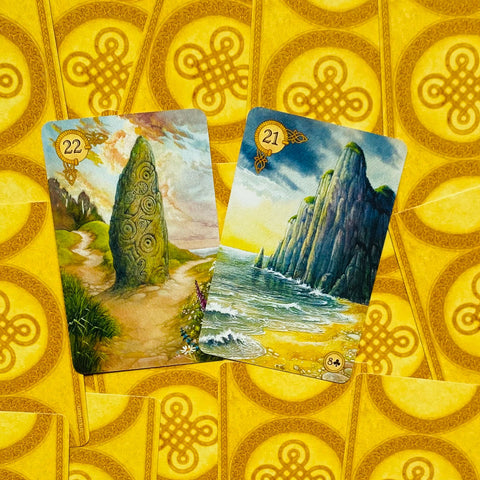 Lenormand kortos su dviem priekiniais paveikslais — jūros krantinė su uola ir menhiris pievų kelyje, geltonos nugarėlės fone