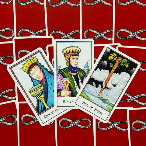 Tarot kortos — trijų kortų išklotinė (Karalienė taurėse, Karalius taurėse, lazdų tūzas) ant raudonų nugarėlių su gyvatės raštu