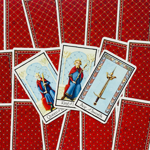Tarot kortos su raudonomis nugarėlėmis, trijose atvertose kortose: Lazdų karalienė, Lazdų karalius ir Kardų tūzas.