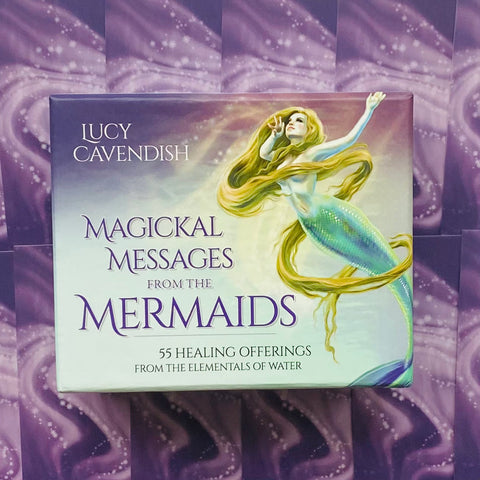 Kortų rinkinys Magickal Messages from the Mermaids, Lucy Cavendish, violetinė priekinė dėžutė su undinės iliustracija, arti konvejerio fone