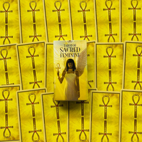 Tarot kortos Tarot of Sacred Feminine geltoname fone, dėžutė su angeliška figūra, kortų nugarėlės aplink