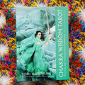 Chakra Wisdom Tarot kortų dėžutė su žalsvu viršeliu, moters figūra laikanti kardą, padėta ant spalvingo audinio fono