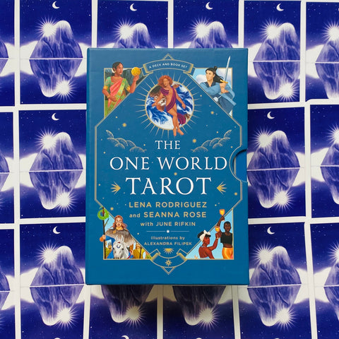 Tarot kortos The One World Tarot mėlyname dėkle su autoriaus vardais ir iliustracijomis, fotografuotos ant mėlyno žvaigždėto kortų fono