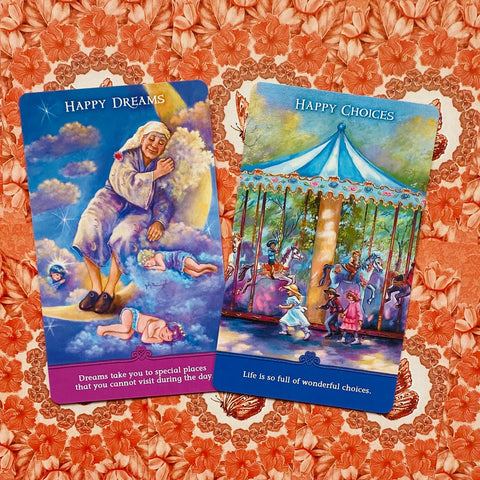 Orakulo kortos: dvi ryškiai mėlynos Happy Dreams ir Happy Choices kortos kampu ant raudono gėlių audinio, pabrėžiančios sapnų ir pasirinkimų temą