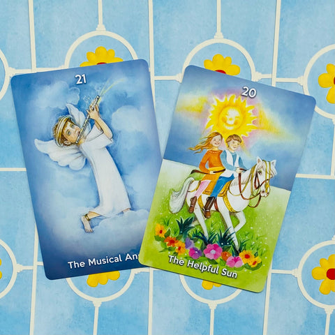 Tarot kortos vaikams, spalvotos iliustracijos: Angelų (21) ir Saulės (20) kortos atverstos kampu ant mėlyno fono