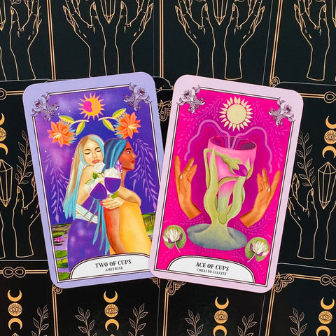 Tarot kortos su dviejų taurų ir taurės tūzo iliustracijomis, violetinė ir rožinė priekinė pusė ant juodo mėnulio ir kristalų fono