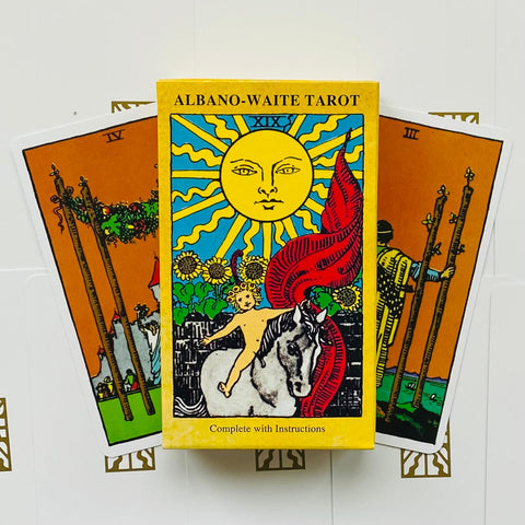 tarot kortos Albano‑Waite geltonoje dėžutėje su Saulės kortos piešiniu, dėžutės priekinė pusė ir dvi išskleistos kortos už jos
