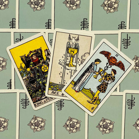 Tarot kortos Rider–Waite stiliaus, atvertos trys kortos (Karalius pentaklių, taurės, tūzas) ant šviesiai mėlyno nugarėlių fono