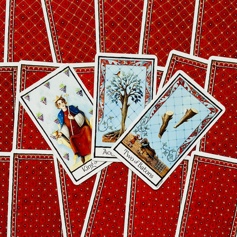 Tarot kortos su raudonomis nugarėlėmis, trys priekinės kortos parodytos arti — išsamios iliustracijos ir ornamentai