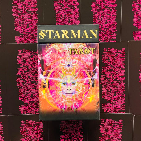 Starman tarot rinkinys su spalvingu psichodeliniu viršeliu ir juodu dangteliu auksiniais užrašais, matomas iš priekio ant rožinių kortų nugarėlių fono
