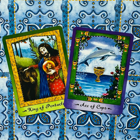 tarot kortos — du atviri kortų pavyzdžiai: King of Pentacles ir Ace of Cups ant mėlyno ornamentuoto fono