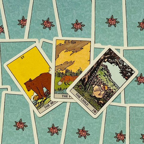 Tarot kortos Rider–Waite stiliaus, trys kortos (Lokys, Lape, Vaikas) išdėstytos kampu ant mėlyno gėlėto nugarėlių fono, viršutinis planas