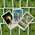 Tarot kortos trys atverstos kortos ant žalių lapų rašto nugarėlių, rodo skirtingus iliustruotus simbolius ir numerius