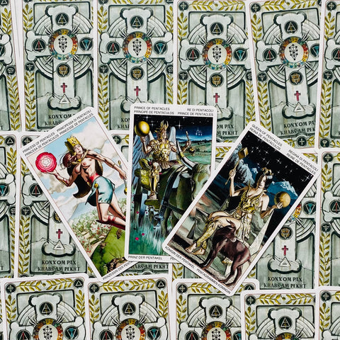 Tarot kortos trijų pentaklių rūmų komplektas — princesė, princas ir karalienė diagoniškai atverstos ant pilkos, ornamentuotos nugarėlės