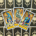 tarot kortos trijų taurų rūšies: Page, Knight ir Queen of Cups su mėlynais‑auksiniais rėmais, išdėstytos ant dekoratyvios nugarėlės fono