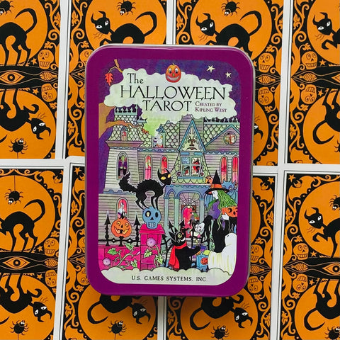 Halloween tarot kortų dėžutė fioletinėje metalinėje skardinėje su siaubo namo iliustracija, padėta ant oranžinių kortų nugarėlių