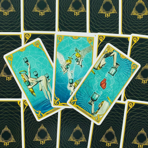 Tarot kortos su mėlynomis taurėmis ir angeliukais — trys atverstos Taurių kortos ant juodai‑aukso nugarėlių, fanuotos