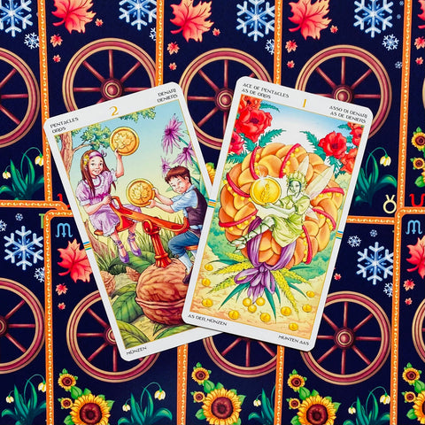 Tarot kortos su spalvingais Pentaklių motyvais — dvi atviros kortos (2 Pentakliai ir Tūzas) ant tamsios nugarėlės rašto