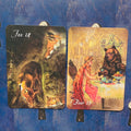 Kortos: dvi iliustruotos oracle kortos šalia viena kitos, Fox (rudi tonai) ir Bear (auksinės bei rožinės detalės), fronto dizainai matomi