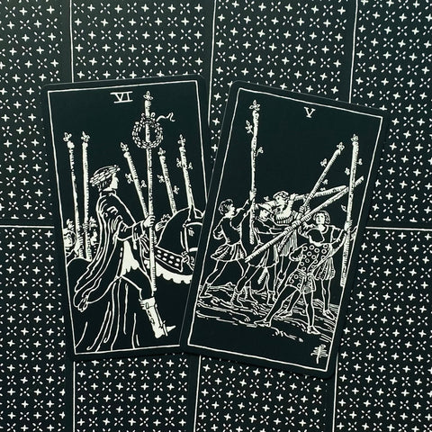 Tarot kortos juodos su baltu piešiniu, dvi atverstos kortos (VI ir V) paryškintos kampu, rodo pergalę ir konfliktą
