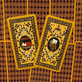 Tarot kortos aukso ir rudos nugarėlės su kryžių ir augaliniu ornamentu, dvi kortos šonu išdėstytos (variantas su III ir IV)