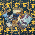 Tarot kortos trijų kortų išklotinė su ornamentuotais auksiniais kraštais ant mėlyno‑geltono fono su geltonais žirgais ir saulėmis, iliustraciniai meniniai paveikslai