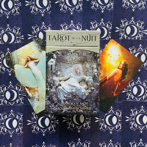 tarot kortos Tarot de la Nuit, centre matoma sidabrinė dėžutė, atverstos dvi iliustruotos kortos ir tamsiai mėlyni nugarėlių raštai