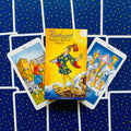 Radiant Rider‑Waite tarot kortų rinkinys geltona dėžutė priekyje, išskleistos taurės kortos ant mėlyno žvaigždėto fono