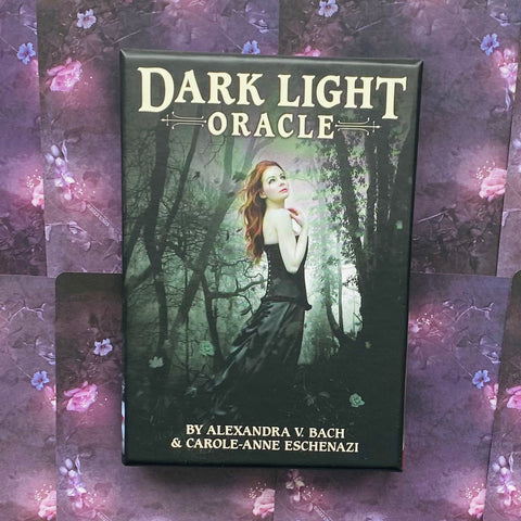 Dark Light Oracle kortų rinkinys juodoje dėžutėje, priekinis vaizdas su raudonplauke moterimi miške ant violetinio gėlėto fono, autoriai apačioje
