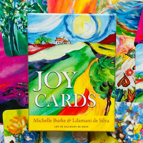 Kortų rinkinys Joy Cards su ryškiais Lilamani de Silva iliustracijų viršeliais, centre matomas spalvingas dėklas, tinkantis dovanai