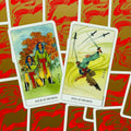 Tarot kortos – dvi atverstos kortos (Four of Swords ir Five of Swords) ant raudonai auksinių nugarėlių fono, parodytos kampu, pabrėžia kortų dizainą