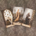 Tarot kortos vintage stiliaus rinkinys su trimis atvertomis Pentaklių kortomis (VIII, IX, X), rodomos iš viršaus ¾ kampu