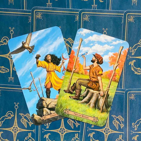 Tarot kortos, dvi atviros kortos — Dvejetai ir Trys lazdelės su rudens pieva ir uolos scenomis ant mėlyno nugarėlių