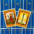 tarot kortos rudos-oranžinės, dvi atverstos ant mėlyno fono — tūzas ir dvejetas stiebų, kortų viršus matomas