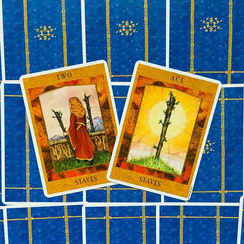 tarot kortos rudos-oranžinės, dvi atverstos ant mėlyno fono — tūzas ir dvejetas stiebų, kortų viršus matomas