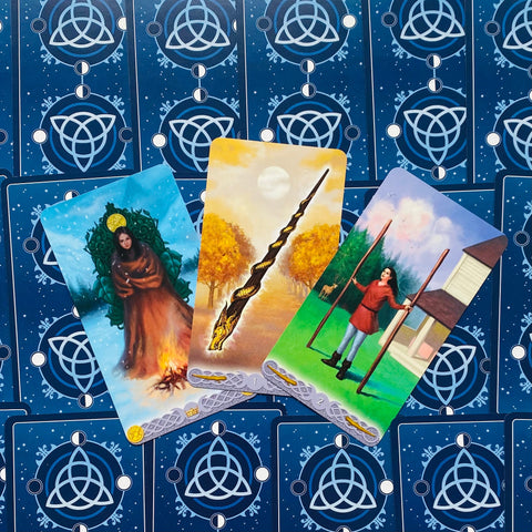Tarot kortos parodytos trijų atverstų kortų komplekte su tamsiai mėlynomis nugarėlėmis ir spalvotais iliustruotais arkanomis