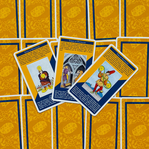 tarot kortos Rider‑Waite stiliaus geltonai mėlynais nugarėliais, trijų Pentaklų kortų išklotinė centre, kampu uždėtos