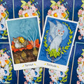 Tarot kortos katėmis, dvi iliustruotos kortos mėlynu fonu (Sprout ir Solitude) ant raštuotos nugarėlės