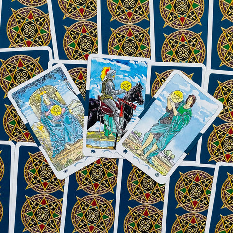 Tarot kortos Rider–Waite komplektas, trys atvertos Pentaklų kortos centre ant tamsiai mėlyno galinio dizaino