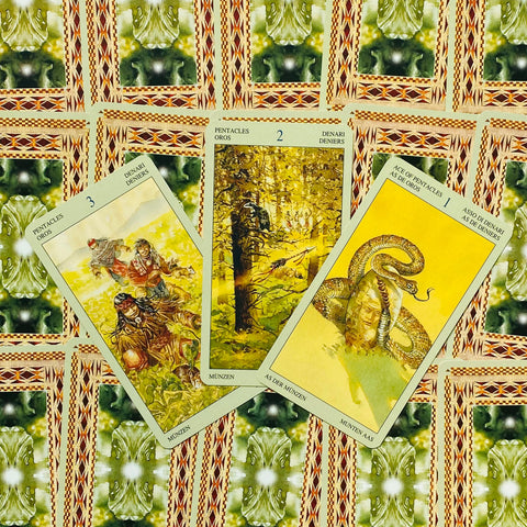 Tarot kortos Wild Unknown pentacles rinkinys: trys geltonos monetų kortos ant žaliai‑raudono ornamentuoto audinio, išdėstytos iš viršaus