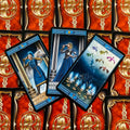 Tarot kortos su mėlynais rėmeliais, trys atverstos kortos (karžygė, dama, dešimt taurų) ant raudono auksuoto nugarėlių fono