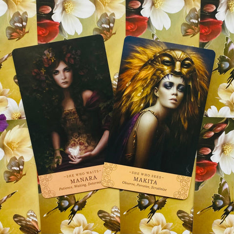 Tarot kortos su dviem kortomis: Manara tamsiame fone laikanti švytintį drugelį ir Makita su auksiniu plunksnų šalmu ant geltono fono