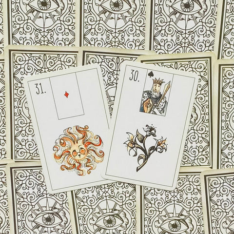 Tarot kortos su ornamentiniu akių raštu nugarėlėse, dvi atverstos kortos (31 deimantėlis ir 30 karalius) matomos iš viršaus, pabrėžiančios skirtingus iliustracijų variantus