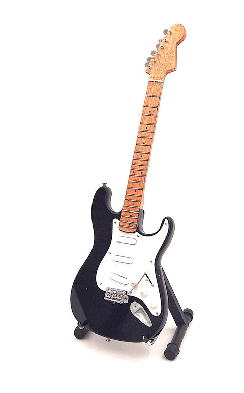 Elektrinė gitara juoda su natūralaus klevo kaklu, Strat stiliaus, pilno ilgio pasvirusi ant stovo, matomos tremolo ir baltas pickguard