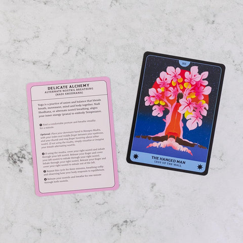 Tarot kortos dviejų pusių rodymas: spalvingas The Hanged Man priekis ir rožinė instrukcijų atgalinė kortelė, plokščias kampas ant marmuro fono