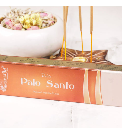Palo Santo smilkalų lazdelės (Aromatika) oranžinėje dėžutėje, uždegtos laikiklyje šalia džiovintų gėlių