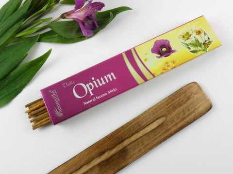 Smilkalai Opium Aromatika rožinėje–geltonoje pakuotėje, atidaryta dėžutė su lazdelėmis ir mediniu laikikliu