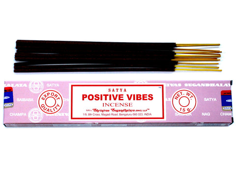 Smilkalai Satya Positive Vibes 15 g rožinėje dėžutėje su tamsiomis kvapniomis lazdelėmis ir geltonais koteliais, išdėstyti virš dėžutės